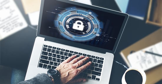Man with hand over keyboard of an open laptop. The laptop rests on a table with documents that are not in focus. The screen on the laptop displays a padlock.